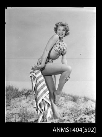 Photographic negative of a swimsuit model posing with a towel on a sand dune