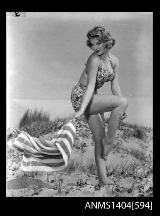 Photographic negative of a swimsuit model posing with a towel on a sand dune