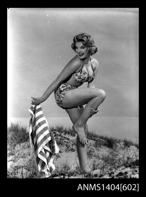 Photographic negative of a swimsuit model posing with a towel on a sand dune