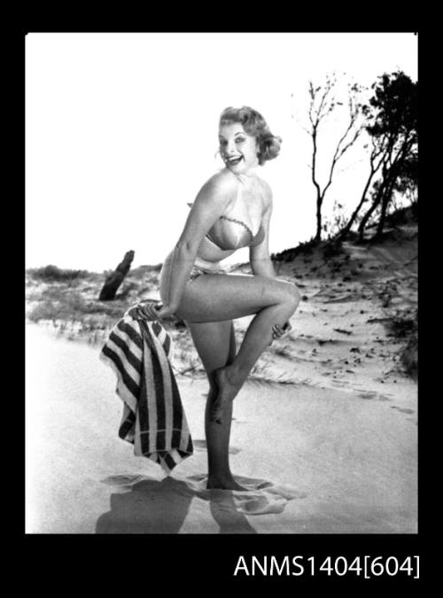 Photographic negative of a swimsuit model posing with a towel on a sand dune