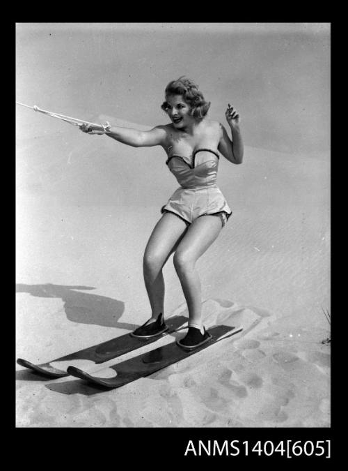 Photographic negative of a swimsuit model posing with skis on a sand dune