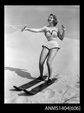 Photographic negative of a swimsuit model posing with skis on a sand dune