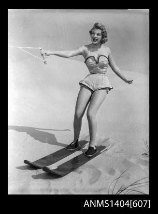 Photographic negative of a swimsuit model posing with skis on a sand dune