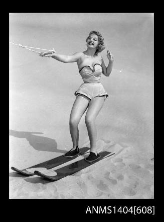 Photographic negative of a swimsuit model posing with skis on a sand dune