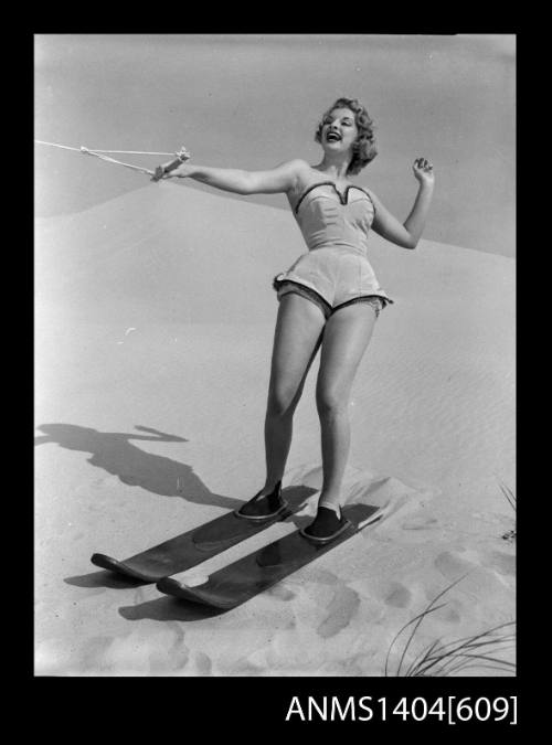 Photographic negative of a swimsuit model posing with skis on a sand dune