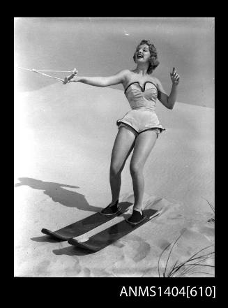 Photographic negative of a swimsuit model posing with skis on a sand dune