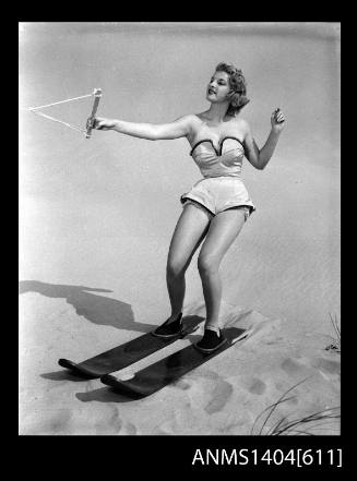 Photographic negative of a swimsuit model posing with skis on a sand dune