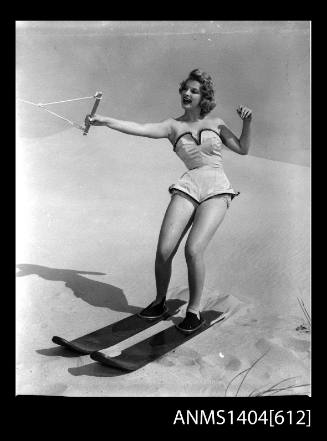 Photographic negative of a swimsuit model posing with skis on a sand dune