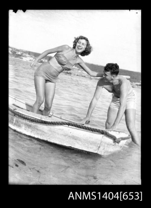 Photographic negative of a man and woman modelling swim wear on a small rowboat