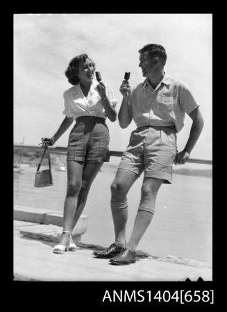 Photographic negative of a man and woman modelling casual wear on a promenade eating icecream