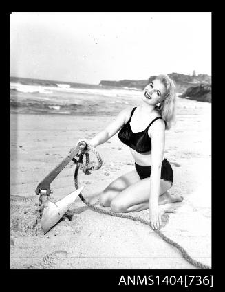 Photographic negative of a swimsuit model posing on a sand dune with an anchor