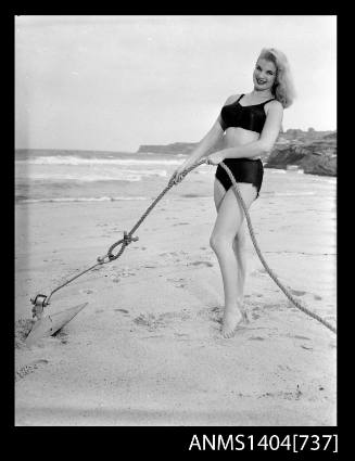 Photographic negative of a swimsuit model posing on a sand dune with an anchor