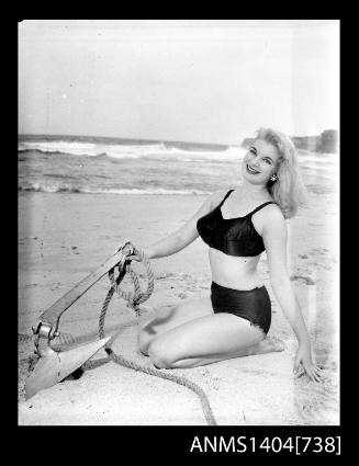Photographic negative of a swimsuit model posing on a sand dune with an anchor