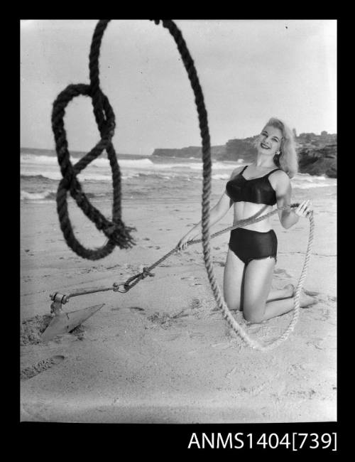 Photographic negative of a swimsuit model posing on a sand dune with an anchor