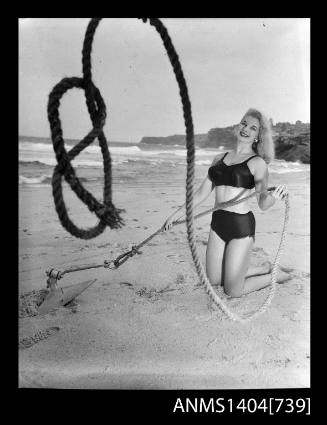 Photographic negative of a swimsuit model posing on a sand dune with an anchor