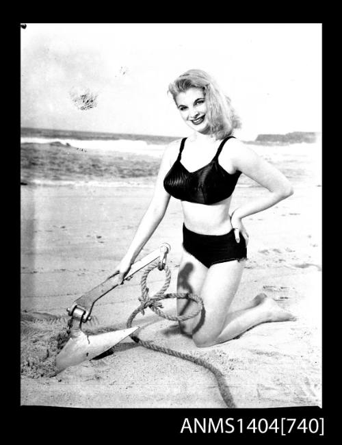 Photographic negative of a swimsuit model posing on a sand dune with an anchor