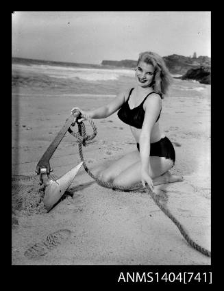 Photographic negative of a swimsuit model posing on a sand dune with an anchor