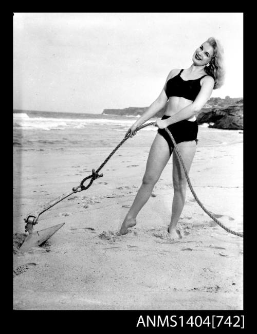 Photographic negative of a swimsuit model posing on a sand dune with an anchor