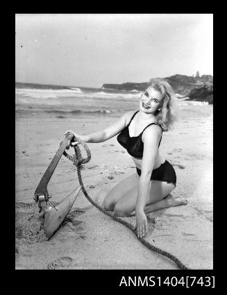 Photographic negative of a swimsuit model posing on a sand dune with an anchor