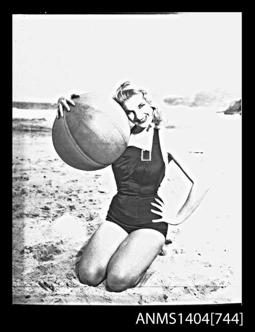 Photographic negative of a swimsuit model posing on a sand dune with a beach ball