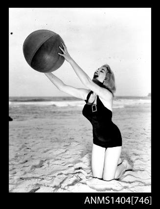 Photographic negative of a swimsuit model posing on a sand dune with a beach ball