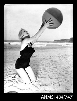 Photographic negative of a swimsuit model posing on a sand dune with a beach ball