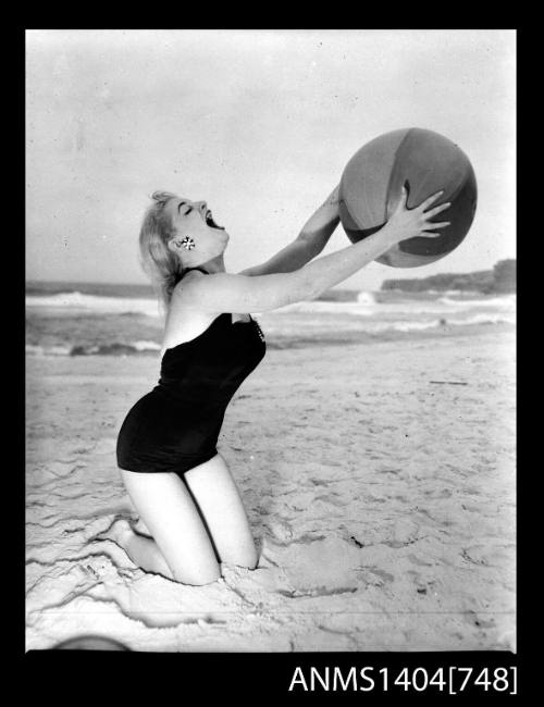 Photographic negative of a swimsuit model posing on a sand dune with a beach ball