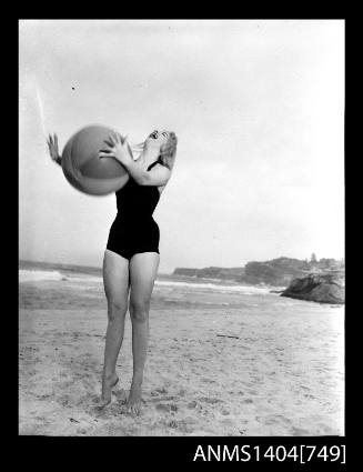 Photographic negative of a swimsuit model posing on a sand dune with a beach ball