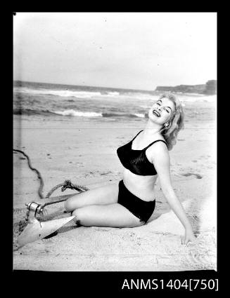 Photographic negative of a swimsuit model posing on a sand dune with an anchor