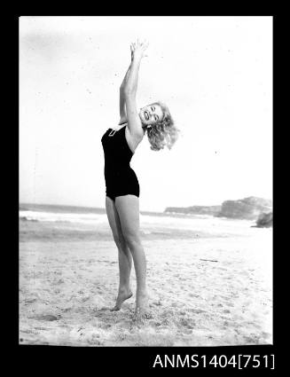 Photographic negative of a swimsuit model posing on a sand dune with a beach ball