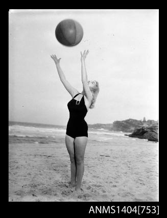 Photographic negative of a swimsuit model posing on a sand dune with a beach ball