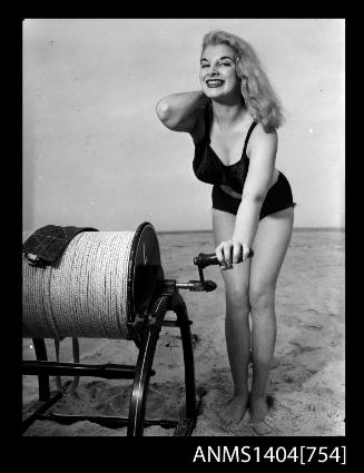 Photographic negative of a swimsuit model posing on a sand dune with a surf reel