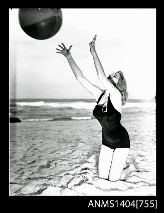 Photographic negative of a swimsuit model posing on a sand dune with a beach ball