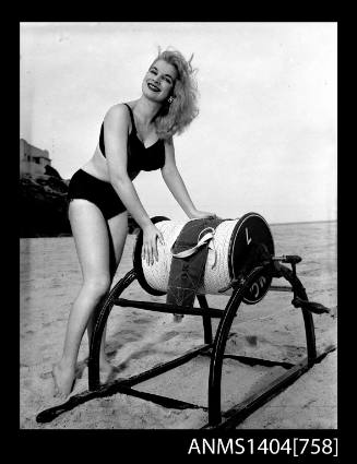 Photographic negative of a swimsuit model posing on a sand dune with a surf reel