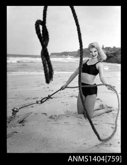 Photographic negative of a swimsuit model posing on a sand dune with an anchor