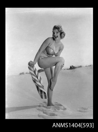 Photographic negative of a swimsuit model posing with a towel on a sand dune