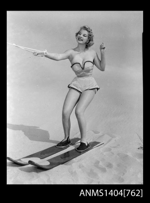 Photographic negative of a swimsuit model posing with skis on a sand dune