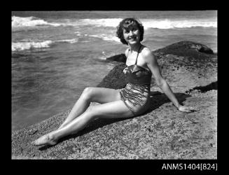 Photographic negative of a swimsuit model posing on a rock