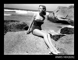 Photographic negative of a swimsuit model posing on a rock