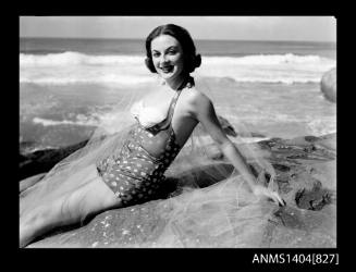 Photographic negative of a swimsuit model posing on a rock