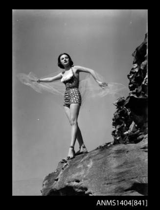 Photographic negative of a swimsuit model posing on a rock