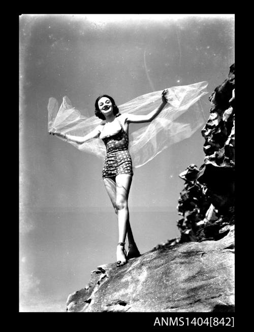 Photographic negative of a swimsuit model posing on a rock