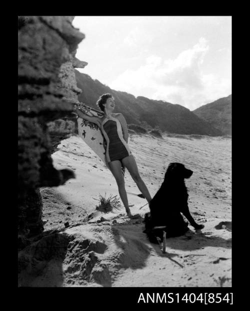 Swimsuit model and dog posing on a beach near a rock