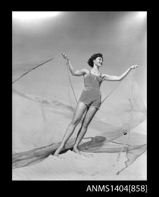 Photographic negative of a swimsuit model posing on a beach with a fishing net