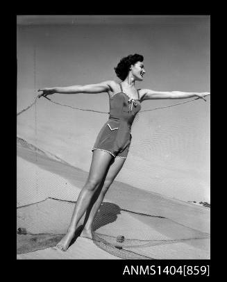 Photographic negative of a swimsuit model posing on a beach with a fishing net