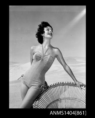 Photographic negative of a swimsuit model posing on a beach with a chair