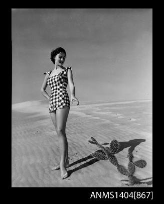 Photographic negative of a swimsuit model posing on a sand dune near a cactus