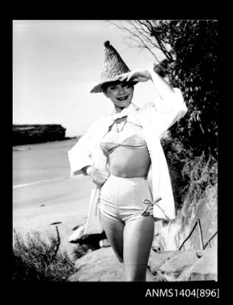 Photographic negative of a swimsuit model posing on a rock near a beach