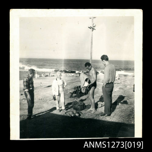 Denis George and three other people on the shoreline, with diving equipment in front of George