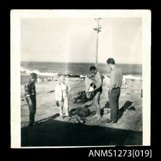 Denis George and three other people on the shoreline, with diving equipment in front of George